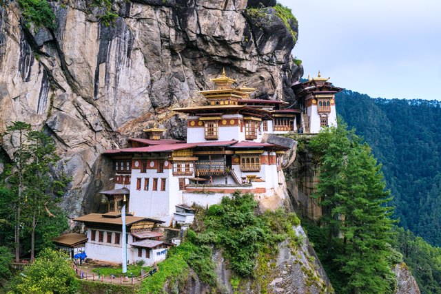 Taktsang Monastery (Tiger’s Nest) perched on a cliffside above Paro Valley, surrounded by Bhutan’s Himalayan mountains and pine forests.