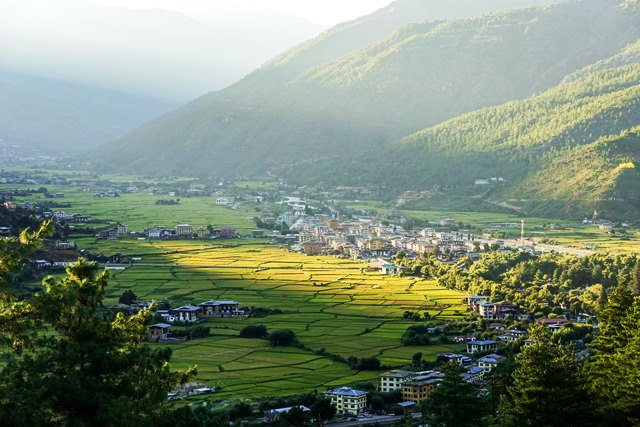 Paro Valley in Bhutan with traditional houses, green fields, Paro Dzong, and Himalayan mountain views.