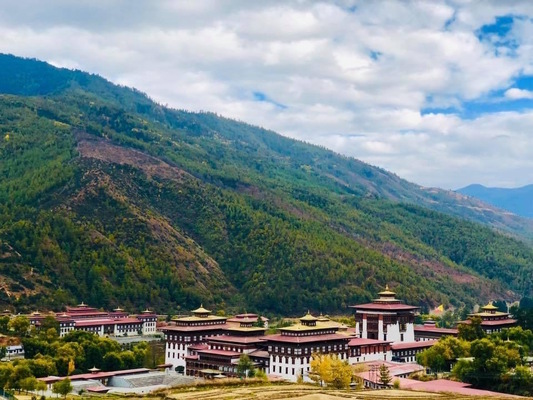 Tashichho Dzong in Thimphu Bhutan with traditional white architecture, golden roofs, prayer flags, and surrounding Himalayan scenery.