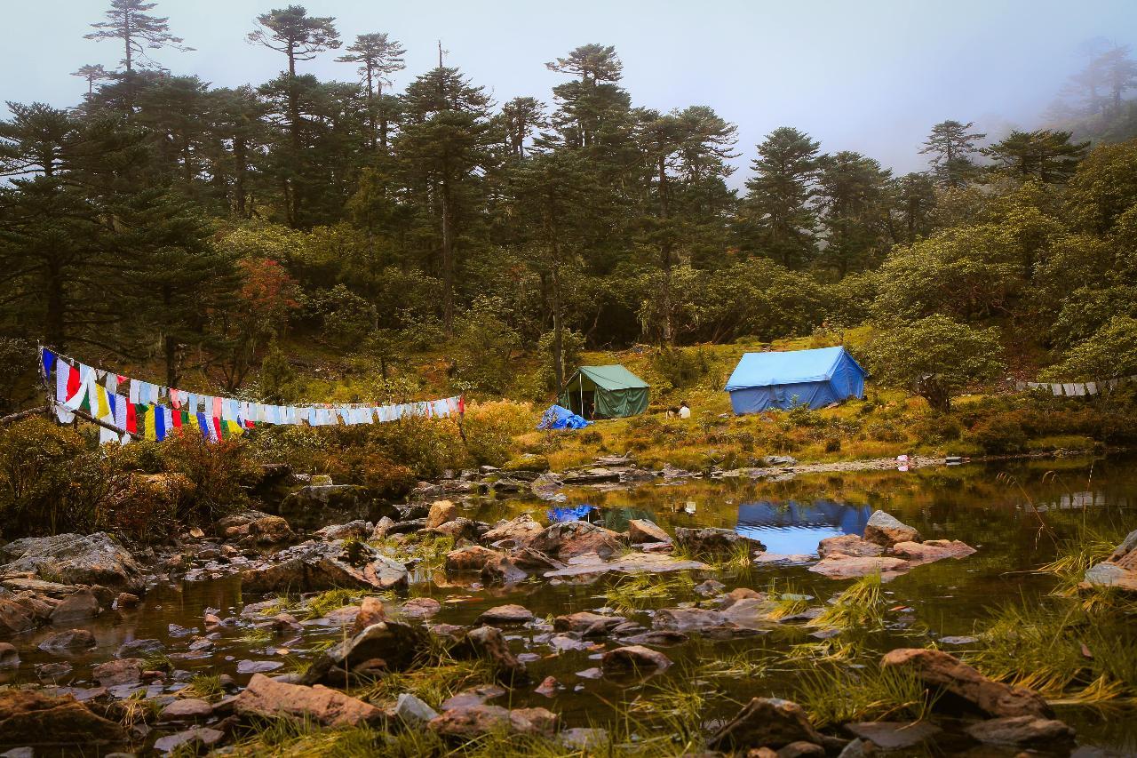 A remote trekking campsite in Bhutan with tents surrounded by lush forests and mountain landscapes.